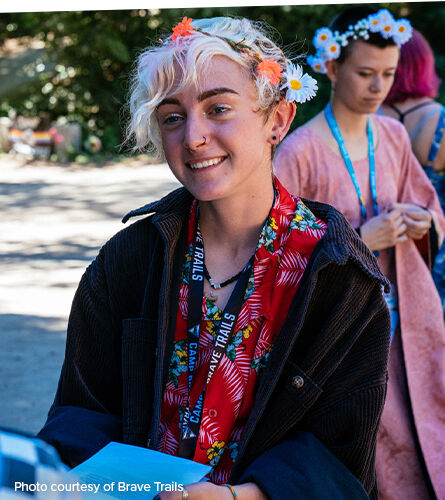 Photo: A person smiling at a community event. Caption: photo courtesy of Brave Trails.